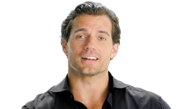 Henry Cavill Breaks Down The Blaviken Fight Scene Shot By Shot: hollywood-Star Henry Cavill sitzt vor einem hellen Hintergrund und erklärt, wie eine Kampfszene in der Netflix-Serie The Witcher entstanden ist.