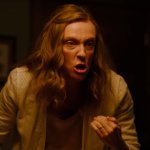 Hereditary: Toni Collette steht in einer Wohnung und wirkt sehr wütend. Ihr Haar ist durcheinander. Das Licht unterstreicht die gespannte Atmosphäre.