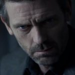 Dr. House: der Schauspieler Hugh Laurie sitzt im Halbdunklen. Die Hälfte seines Gesichts ist von einem Schatten bedeckt. Er wirkt besorgt.