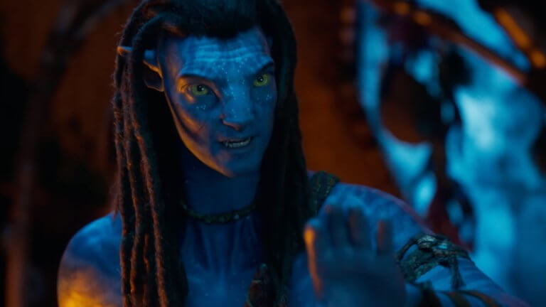 Avatar: Fire and Ash: Ein außerirdisches Wesen mit blauer Hand und humanoiden Zügen in einer durch ein Lagerfeuer erhellten Höhle.