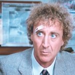 Die Frau in Rot: Gene Wilder sitzt im Büro und macht sich Gedanken. Er trägt einen grauen Anzug und hat ein Pflaster über dem rechten Auge.