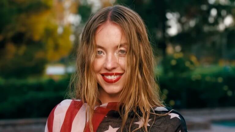 EUPHORIA Staffel 3: Sydney Sweeney steht in einem Garten, trägt die US-Flagge als Oberteil und ihre Haare sind etwas durcheinander.