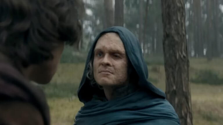 House of the Dragon | S3 - EP.2: eine Gestalt mit Kapuze, mit starken Brandnarben, steht im Wald und wirkt unzufrieden.