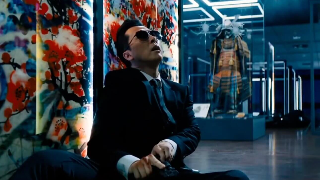 John Wick 4: Donnie Yen als Caine, sitzt vor einem bunten Kunstwerk und lädt seine Pistole. Im Hintergrund sind weitere Kunstwerke zu sehen.