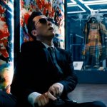 John Wick 4: Donnie Yen als Caine, sitzt vor einem bunten Kunstwerk und lädt seine Pistole. Im Hintergrund sind weitere Kunstwerke zu sehen.