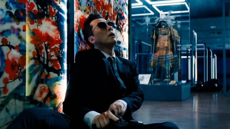 John Wick 4: Donnie Yen als Caine, sitzt vor einem bunten Kunstwerk und lädt seine Pistole. Im Hintergrund sind weitere Kunstwerke zu sehen.
