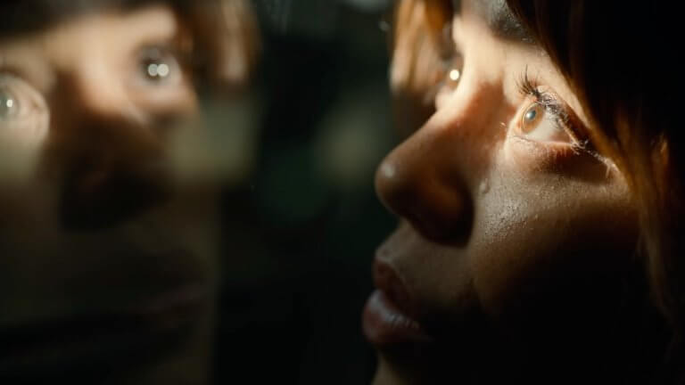 KLARA AND THE SUN: die von Jenna Ortega gespielte Figur namens Klara blickt durch ein Fenster. Ihr Spiegelbild ist in der Glasscheibe zu erkennen.