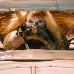 Mad Max: Fury Road: ein Bösewicht in typischer Endzeit-Montur sitzt am Steuer seines Fahrzeugs und blickt entschlossen auf die Straße.
