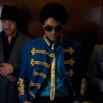 Michael: Michael Jackson steht mit seiner Crew im Aufzug. Er trägt ein auffälliges Oberteil, das an einen Zirkusdirektor erinnert.