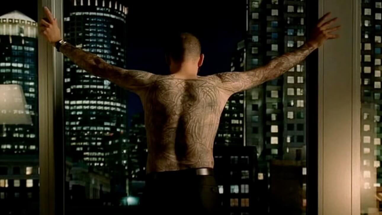 Prison Break: ein tätowierter Mann steht vor dem Fenster mit ausgestreckten Armen. Die Kamera zeigt seinen tätowierten Rücken. Im Hintergrund ist die Skyline einer Stadt zu erkennen.