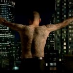 Prison Break: ein tätowierter Mann steht vor dem Fenster mit ausgestreckten Armen. Die Kamera zeigt seinen tätowierten Rücken. Im Hintergrund ist die Skyline einer Stadt zu erkennen.