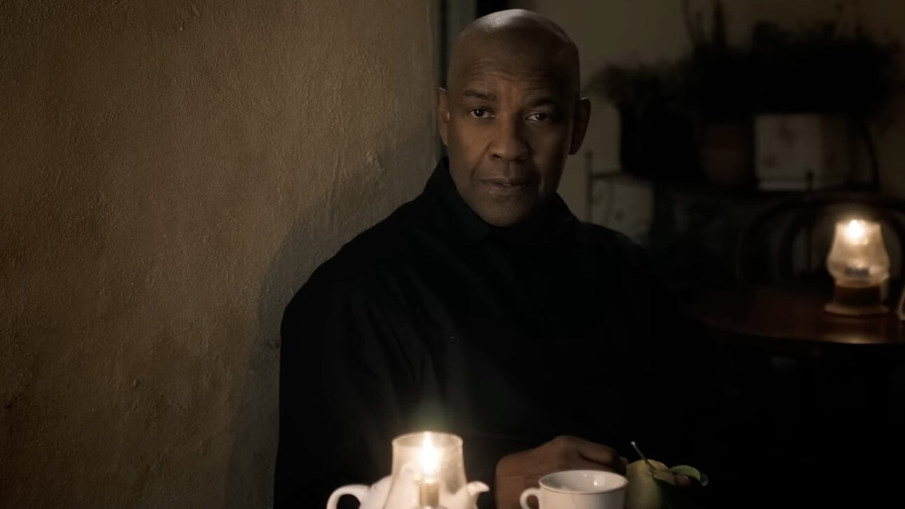 THE EQUALIZER 3: Denzel Washington sitzt an einem Kaffeetisch und trägt ein schwarzes Hemd.