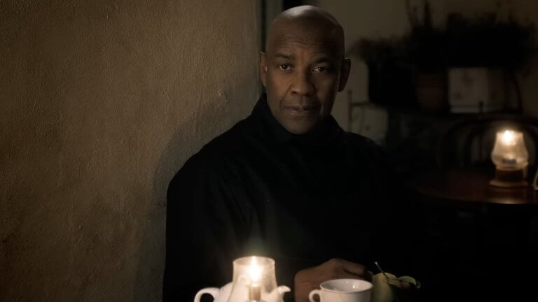 THE EQUALIZER 3: Denzel Washington sitzt an einem Kaffeetisch und trägt ein schwarzes Hemd.