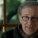 Spielberg (2017) HBO Documentary: Steven Spielberg sitzt vor einem Fenster. Im Hintergrund ist verschwommen ein Garten zu erkennen. Er trägt eine Brille und einen Schal.