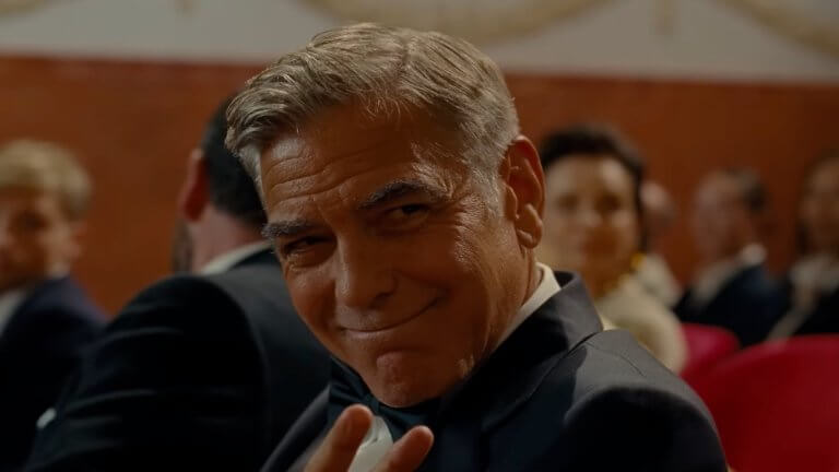 Jay Kelly: George Clooney trägt einen Smoking und grüßt freundlich eine Person, die nicht im Bild ist.