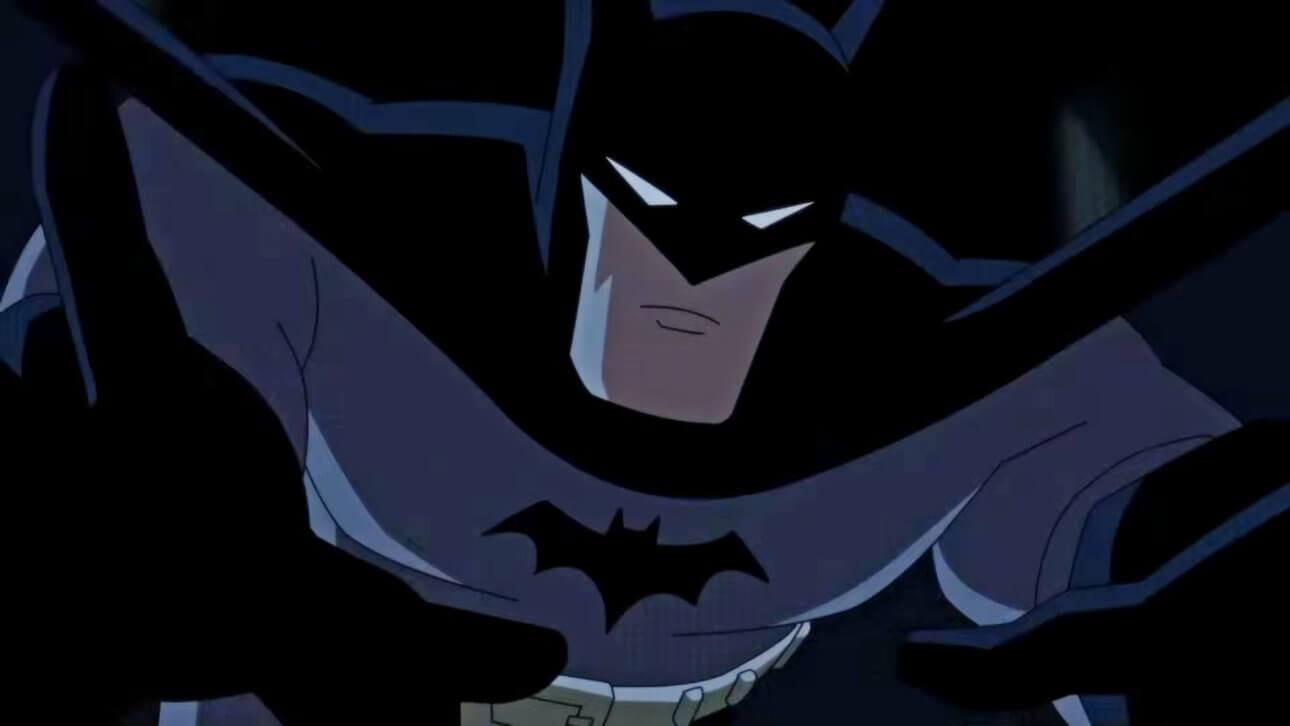 Batman springt mit ausgestreckten Händen nach vorne. Dabei trägt er ein klassisches grau-schwarzes Kostüm und streckt sein markantes Kinn nach vorn.