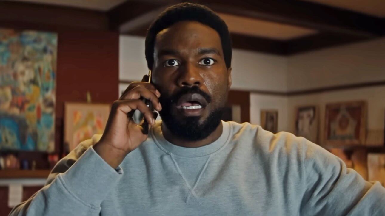 Yahya Abdul-Mateen II telefoniert in der Rolle des Simon Williams und blickt überrascht. Im Hintergrund ist ein Raum mit mehreren Gemälden zu erkennen.