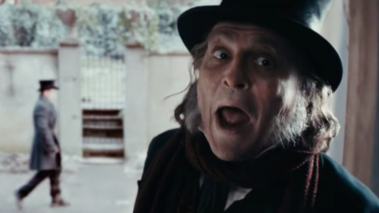 Ebenezer: Johnny Depp als Ebeneezer Scrooge steht vor einem Hauseingang. Im Hintergrund ist verschwommen ein Passant zu erkennen.