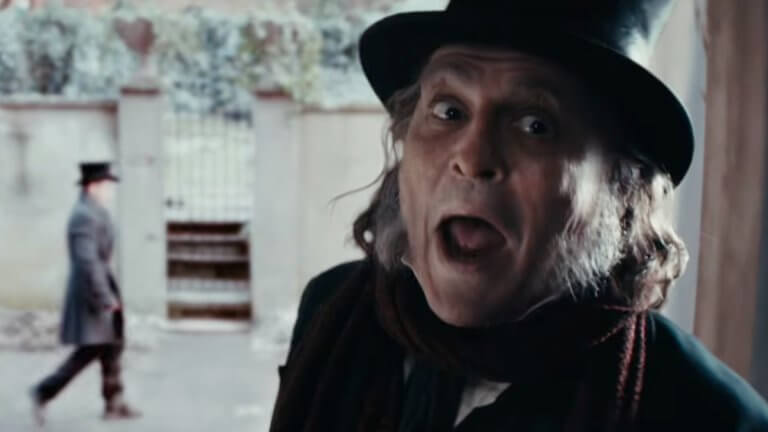 Ebenezer: Johnny Depp als Ebeneezer Scrooge steht vor einem Hauseingang. Im Hintergrund ist verschwommen ein Passant zu erkennen.