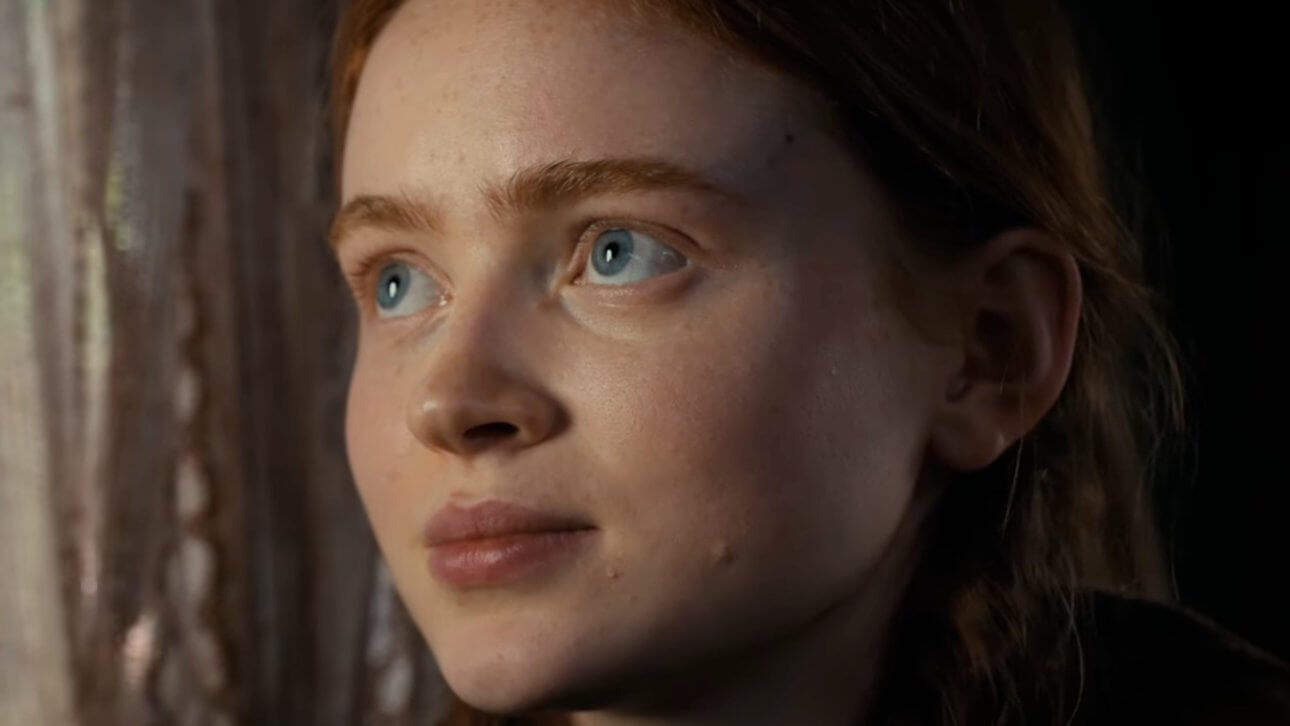 Stranger Things: Sadie Sink blickt durch das Fenster. Neben ihr sind beige Gardinen zu sehen.