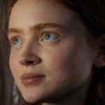 Stranger Things: Sadie Sink blickt durch das Fenster. Neben ihr sind beige Gardinen zu sehen.
