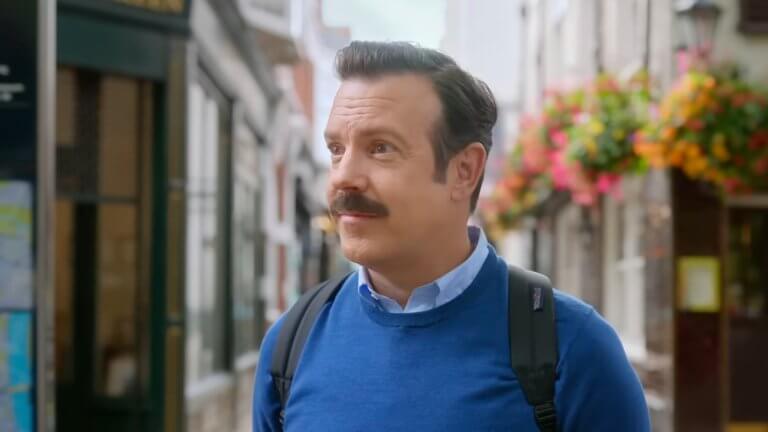 Ted Lasso — Season 4 Official Teaser: Jason Sudeikis als Ted Lasso trägt einen Rucksack und ein blaues Sweatshirt.