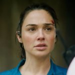 The Runner: Gal Gadot wirkt sichtlich mitgenommen. Sie trägt ein verschmutztes Oberteil in blauer Farbe. Ihr gegenüber erkennt man die Umrisse von zwei britischen Polizisten.