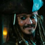 Johnny Depp als Jack Sparrow lächelt in Richtung Kamera. Er trägt den ikonischen Dreispitz und einige Goldzähne blitzen beim Lächeln auf.