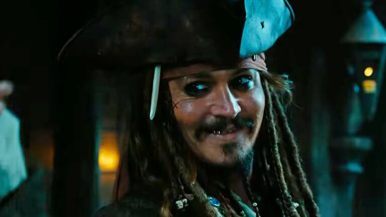 Johnny Depp als Jack Sparrow lächelt in Richtung Kamera. Er trägt den ikonischen Dreispitz und einige Goldzähne blitzen beim Lächeln auf.