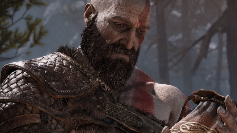 Kratos blickt traurig auf einen Beutel in seinen Händen. Er trägt eine Lederrüstung und ein langer Bart sowie die ikonischen roten Tattoos zieren sein Gesicht.