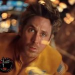 Ryan Gosling schaut nervös zur Kamera. Eine Fensterscheibe vor seinem Gesicht sorgt für die Spiegelung vieler kleiner Lichter. Er trägt eine orangfarbene Astronautenuniform.