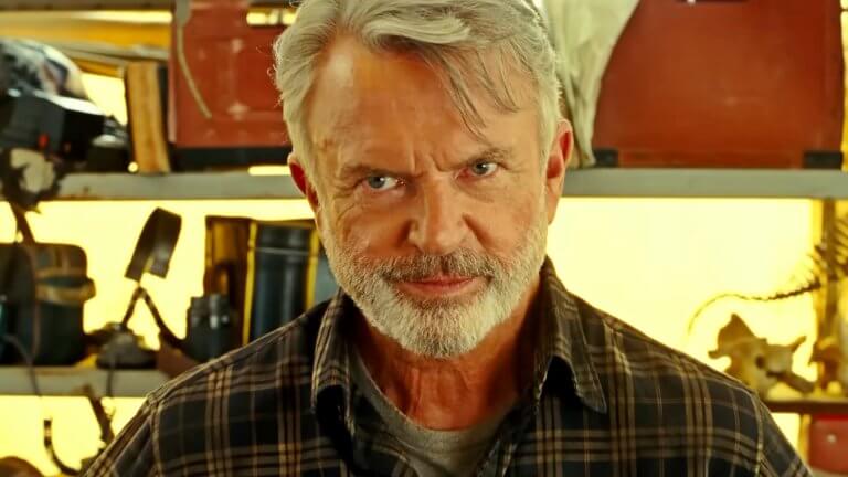 Sam Neill blickt als Dr. Alan Grant teils lächelnd, teils besorgt in Richtung Kamera. Hinter ihm ist ein regal voller archäologischer Werkzeuge zu erkennen.