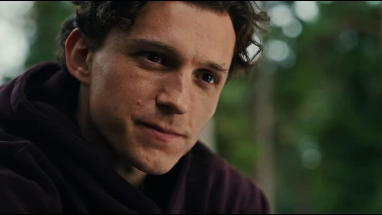 Nahaufnahme von Tom Holland als Peter Parker, der in einem dunklen Hoodie nachdenklich und mit einem subtilen, leicht melancholischen Lächeln an der Kamera vorbeiblickt.