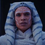 Rosario Dawson blickt als Ahsoka Tano in Richtung Kamera. Sie trägt einen grauen Umhang über einer weißen Robe.