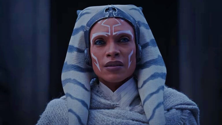 Rosario Dawson blickt als Ahsoka Tano in Richtung Kamera. Sie trägt einen grauen Umhang über einer weißen Robe.