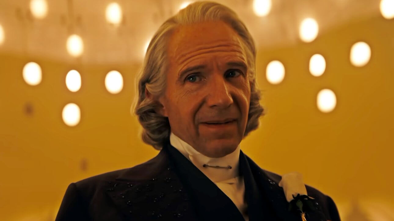 Ralph Fiennes blickt als Präsident Snow mit gerunzelter Stirn zur Seite. Erträgt einen feinen Anzug und die markante weiße Rose am Revers.