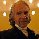 Ralph Fiennes blickt als Präsident Snow mit gerunzelter Stirn zur Seite. Erträgt einen feinen Anzug und die markante weiße Rose am Revers.
