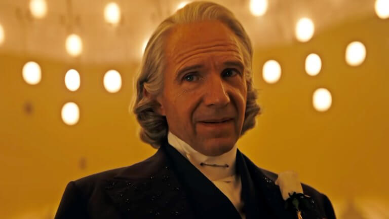 Ralph Fiennes blickt als Präsident Snow mit gerunzelter Stirn zur Seite. Erträgt einen feinen Anzug und die markante weiße Rose am Revers.