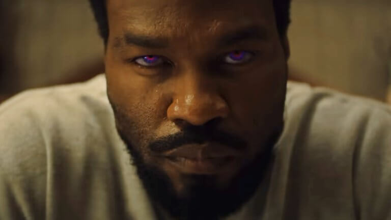 Yahya Abdul-Mateen II blickt in der Rolle von Simon Williams ernst in die Kamera. Seine Augen leuchten in einem intensiven Violett.