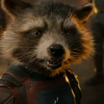 Der modifizierte Waschbär Rocket Raccoon blickt entschlossen in Richtung Kamera. Hinter ihm stehen drei Personen und es brennen einige Feuer.
