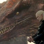 Prinz Daemon steht neben seinem Drachen Caraxes vor einer felsigen Landschaft. Im Hintergrund ist ein abendlicher Himmel zu sehen.