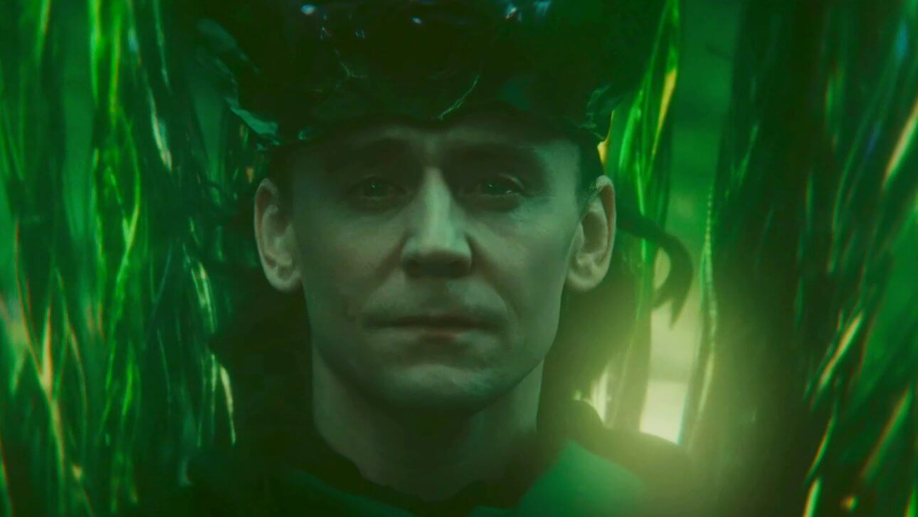 Loki blickt mit ernstem Gesicht und Tränen in den Augen in die Kamera. Seine Umgebung ist erfüllt von leuchtendem Grün und er trägt eine Variante seiner klassichen Krone.