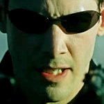 Neo zielt mit zwei Pistolen. Er trägt einen dunklen Mantel und die ikonische Sonnenbrille. Sein Gesichtsausdruck ist angespannt und grimmig.