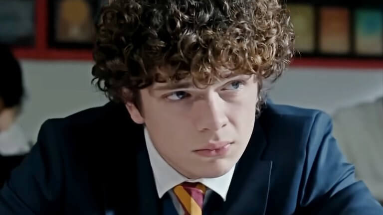 Noah Jupe blickt mit einem unergründlichen Gesichtsausdruck zur Seite. Er trägt eine Schuluniform und hinter ihm sitzen Klassenkameraden.