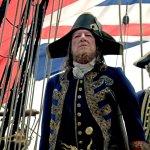 Geoffrey Rush steht als Captain Hector Barbossa in einer prunkvollen Uniform an Bord eines Schiffes. Hinter ihm ist die britische Flagge zu sehen.