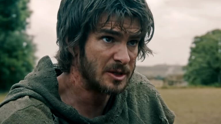 Andrew Garfield als Ploughman steht in dreckiger Kleidung auf einer Wiese. Sein Gesicht ist gezeichnet von Dreck und Entbehrungen.