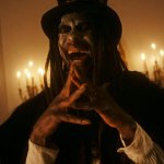 Der Vodoo-Meister Papa Legba lacht manisch und legt die Fingerspitzen aneinander. Seine Augen leuchten blutrot, während der Raum, in dem er steht, von alten Lampen an der Wand erhellt wird.