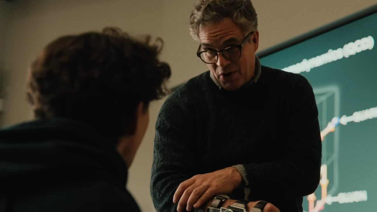 Bruce Banner zeigt Peter Parker seinen Inhibitorchip, der ihn davon abhält zum Hulk zu werden. Im Hintergund ist ein Vorlesungssaal zu erkennen.
