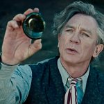 Der Magier, gespielt von Daniel Craig, hält den zerbochenen Boden einer Flasche hoch und blickt fasziniert hindurch. Er trägt Hemd, Krawatte und Weste.