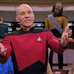 Das Bild zeigt Captain Jean-Luc Picard in einer Uniform auf der Brücke der Enterprise, während er gestikulieren spricht. Im Hintergrund sind weitere Crewmitglieder wie Worf und Counselor Troi zu sehen.